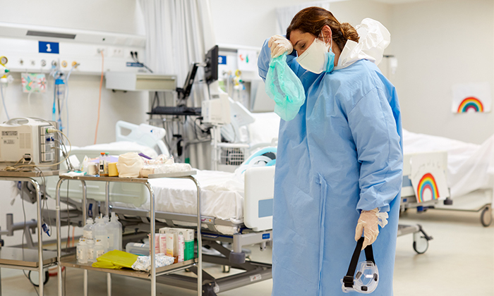 Image d’une travailleuse de la santé en milieu hospitalier portant un équipement de protection individuelle, qui semble épuisée.
