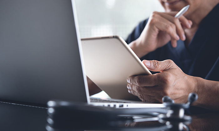 Image d’une personne qui tient une tablette et un stylet en regardant l’écran d’un ordinateur portable.