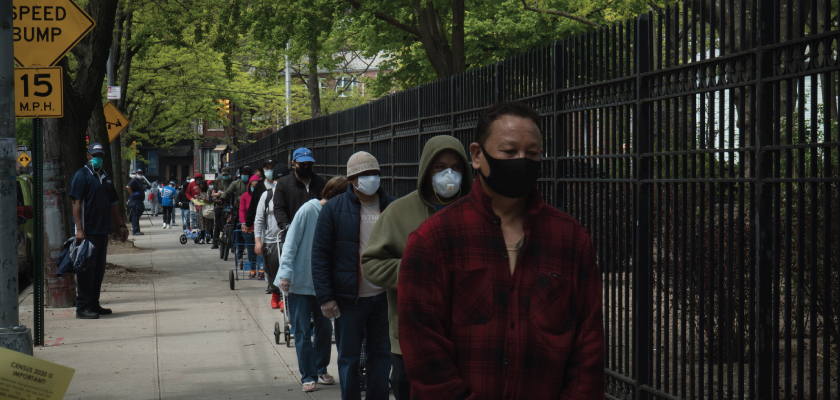 people in masks lining up on the sidewalk